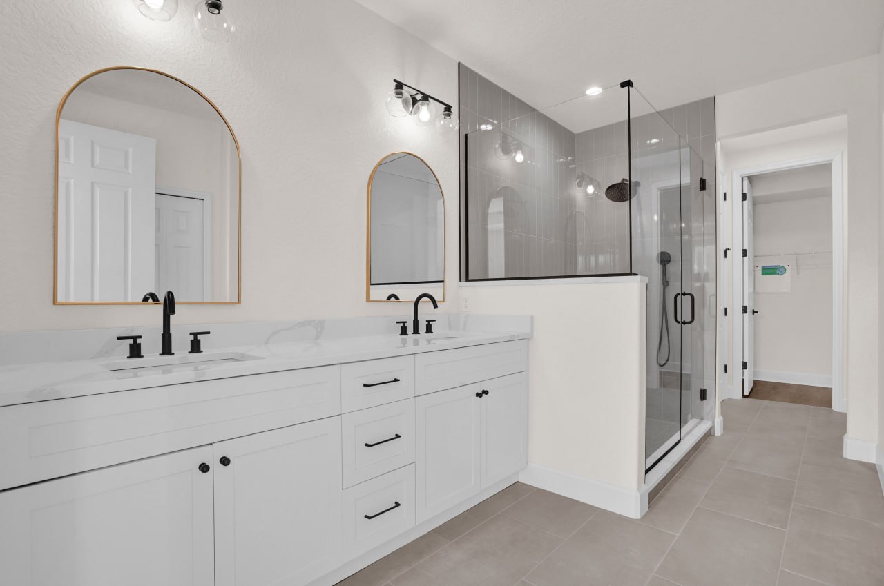 A renovated bathroom with a double vanity, arched mirrors, and a glass-enclosed shower.