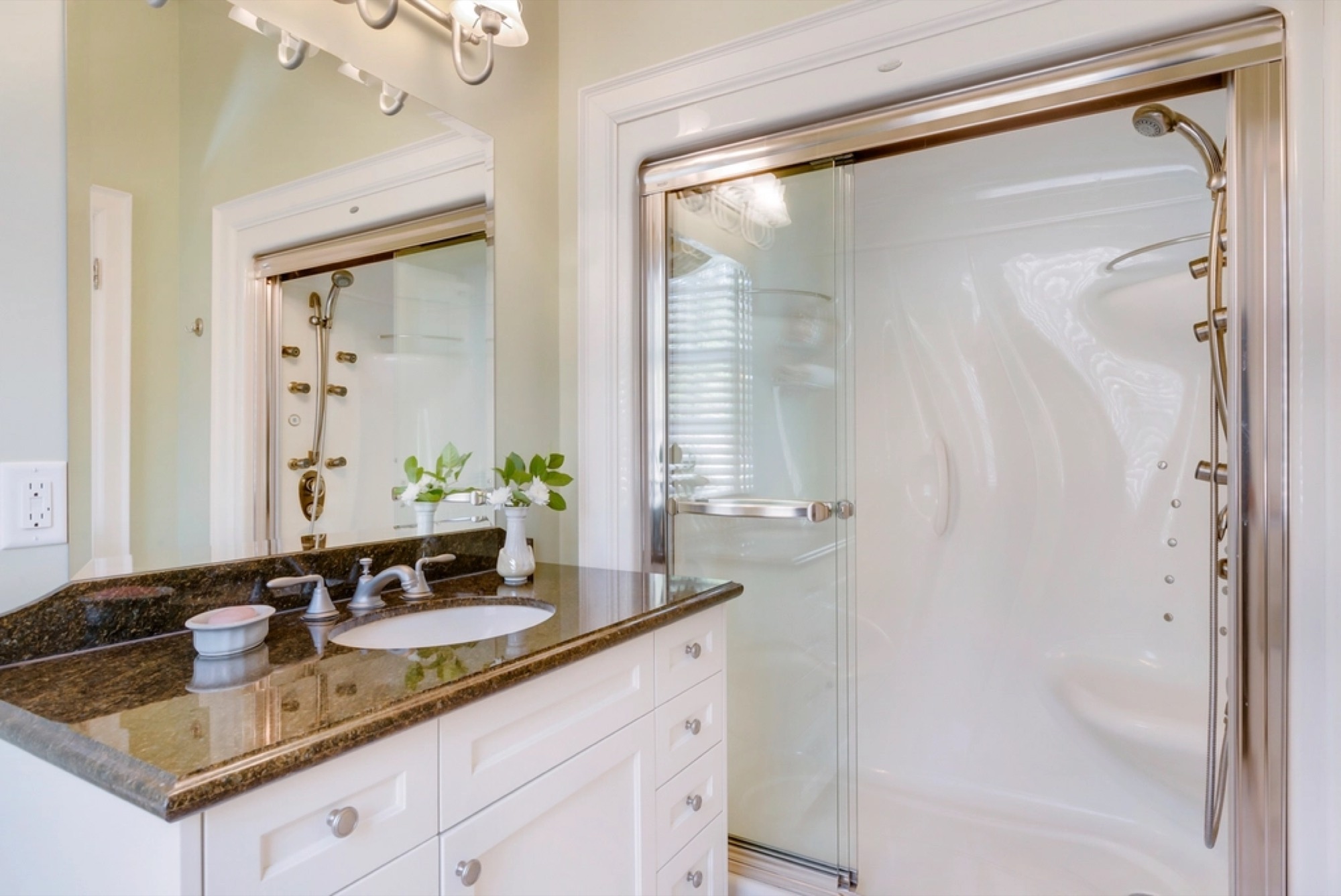 A bathroom vanity with a granite top and a glass shower behind.