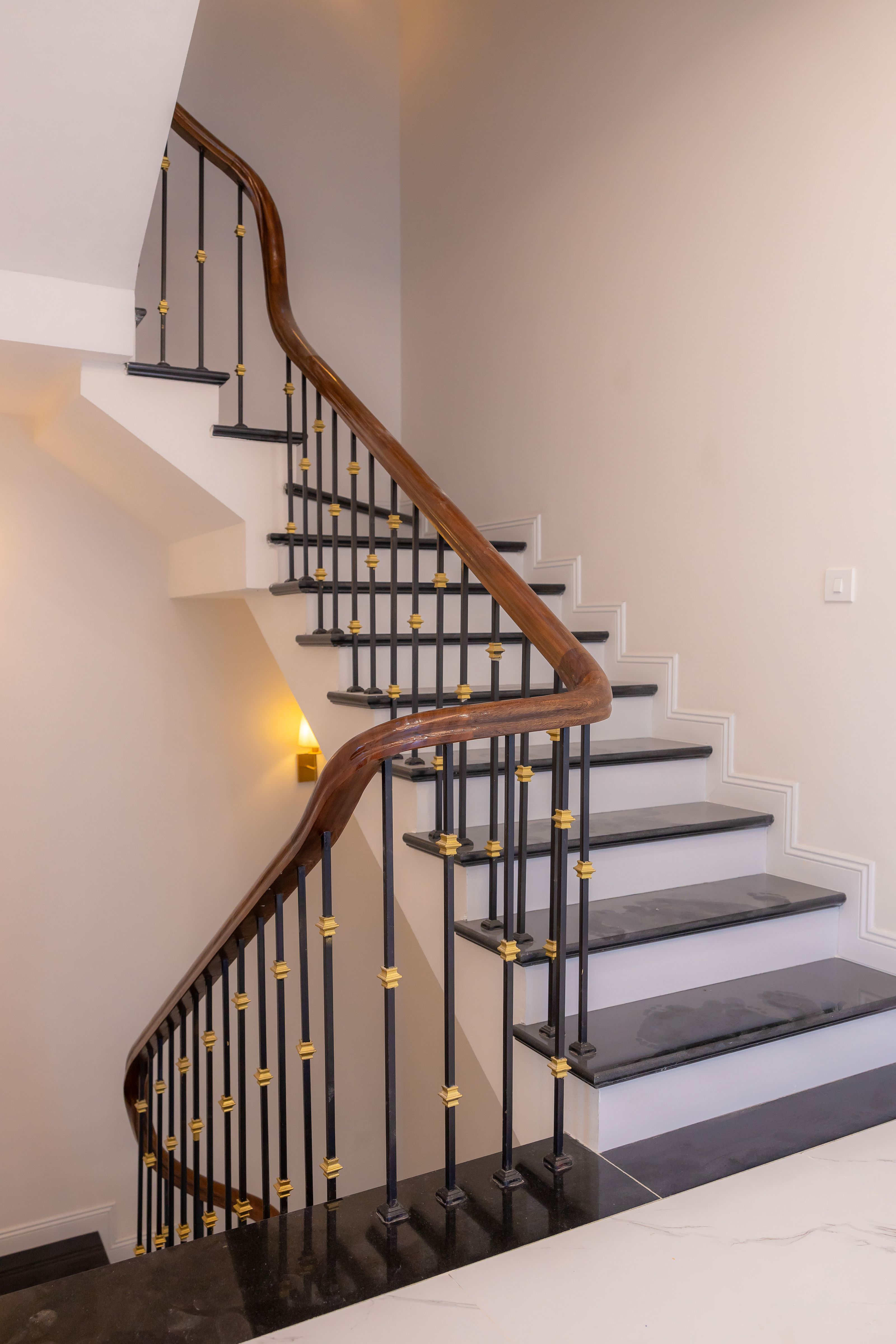An elegant staircase with a curved wood handrail, black balusters, brass details, and crisp white trim.