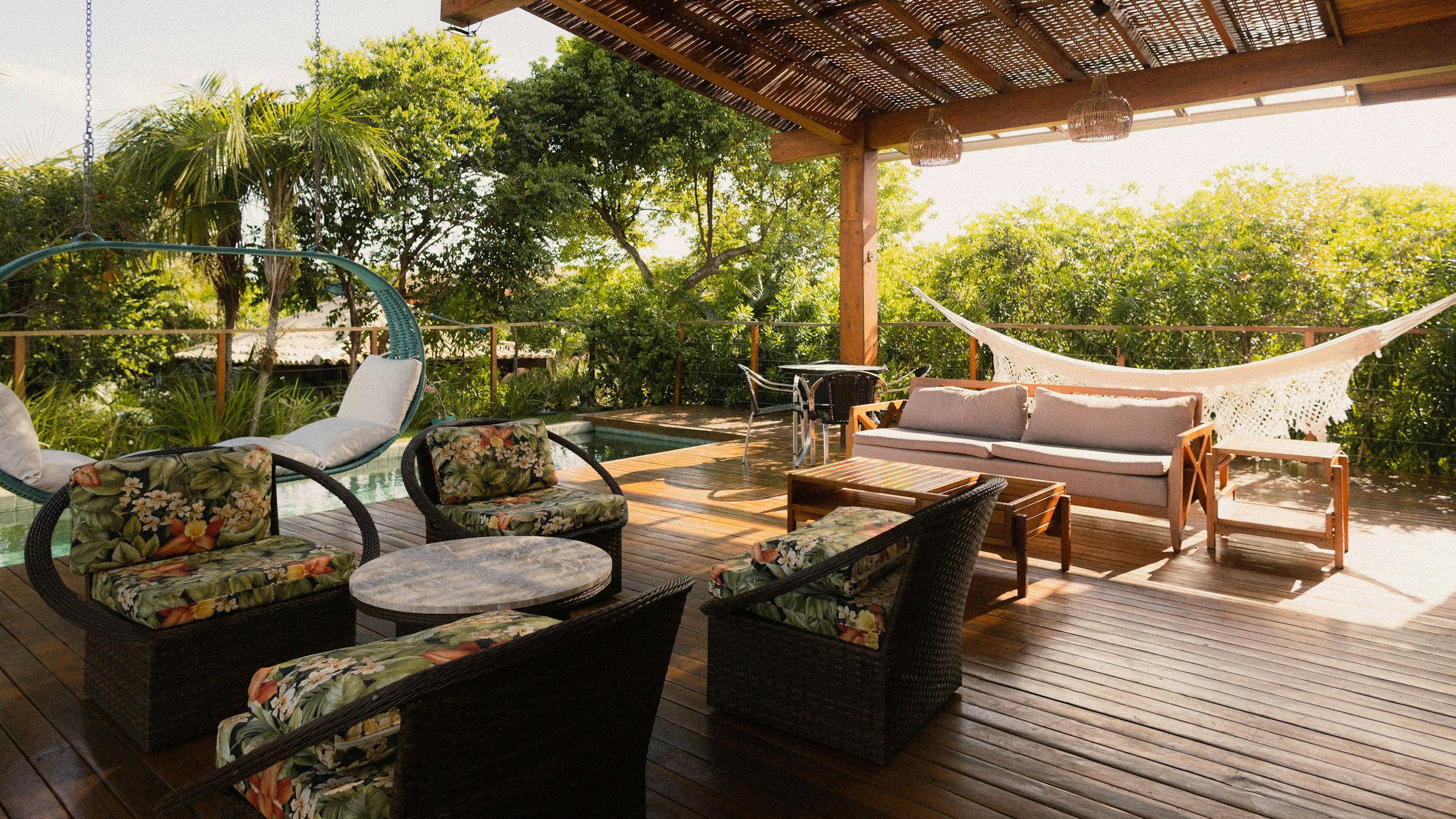 A covered outdoor living area with a wood deck, pool, hammock, and tropical landscaping.