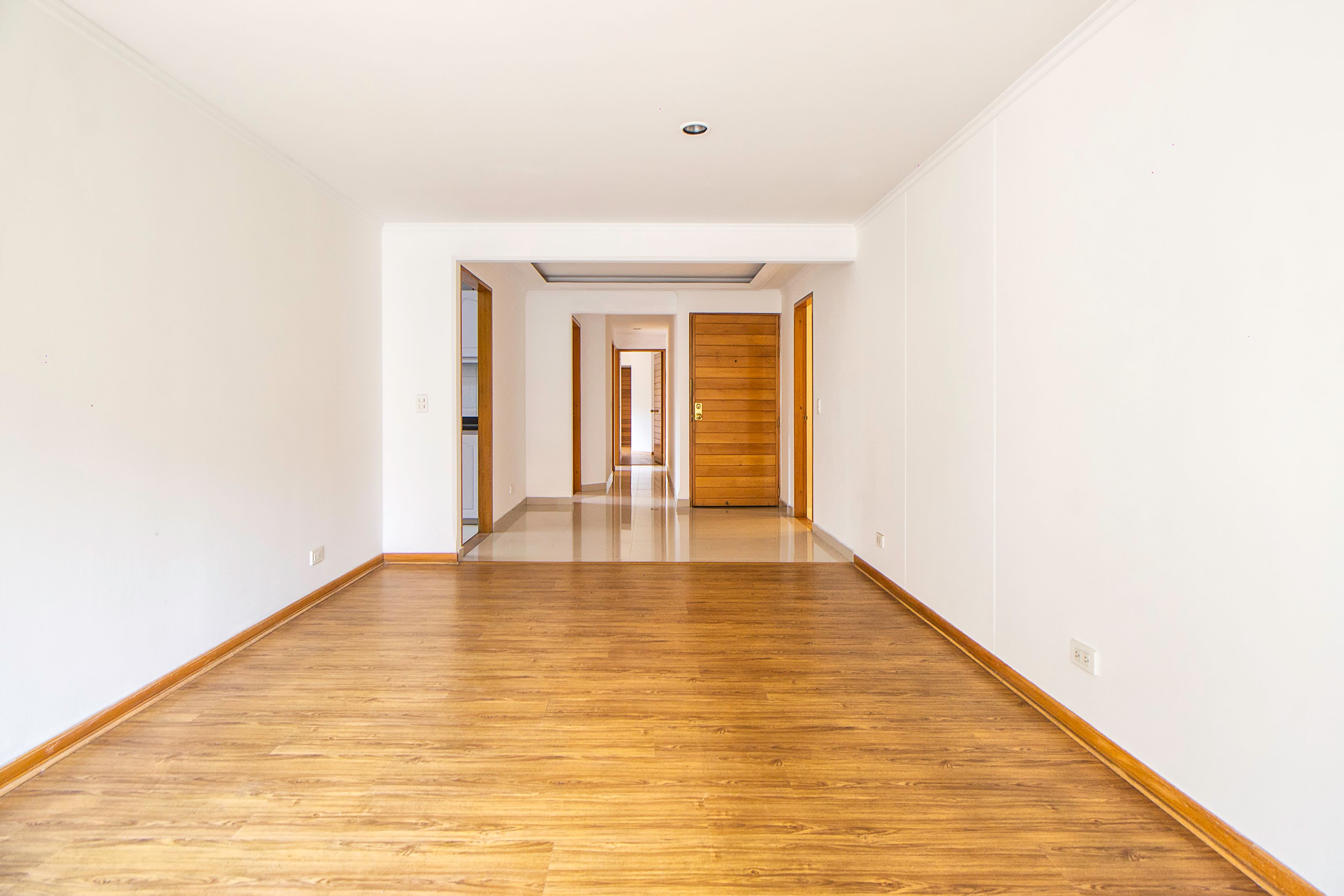 A bright, freshly finished interior with white walls, warm wood flooring, trim, and wood doors.