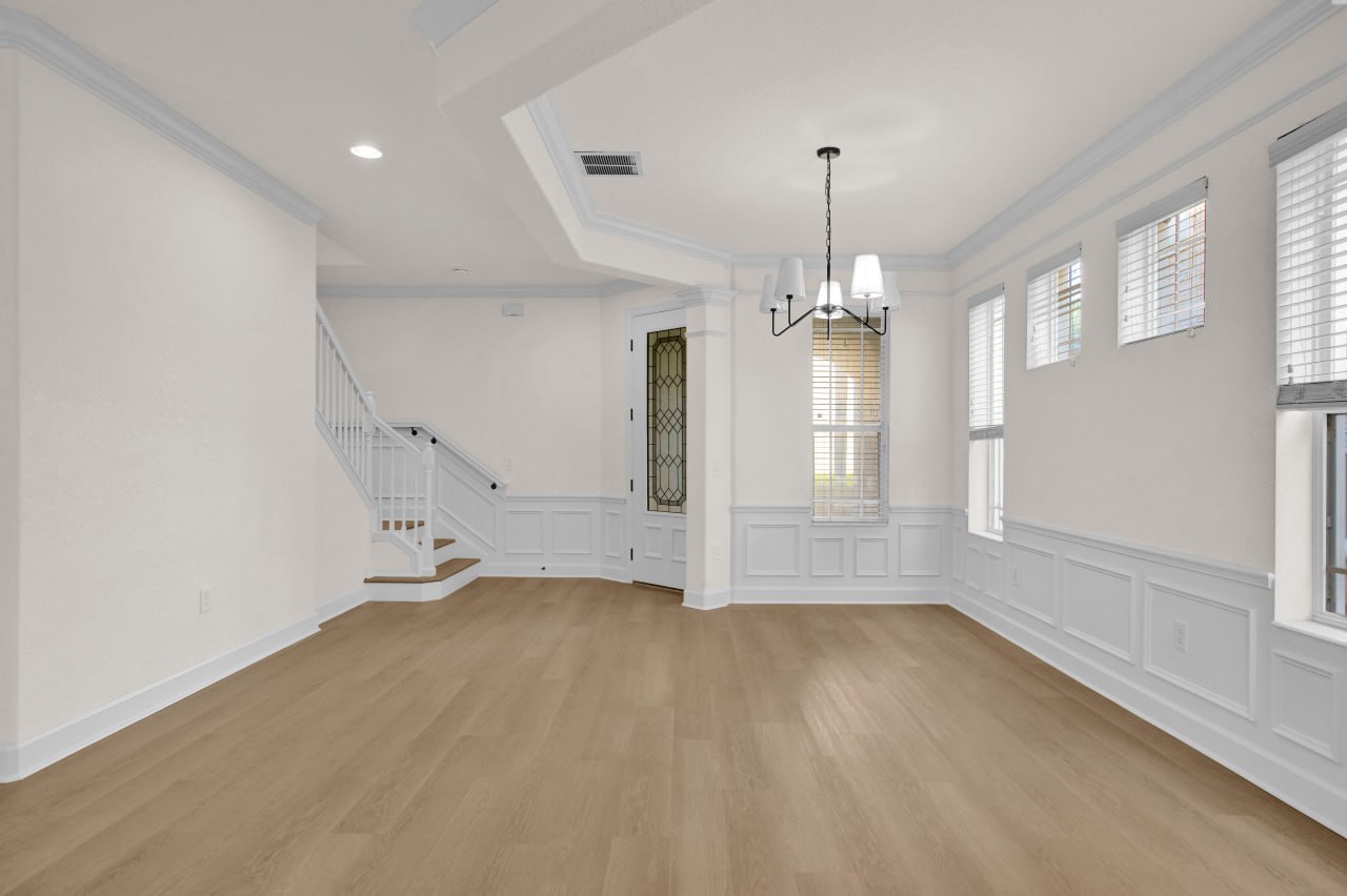 A renovated living space with light wood flooring, decorative wall paneling, tall windows, and a staircase.