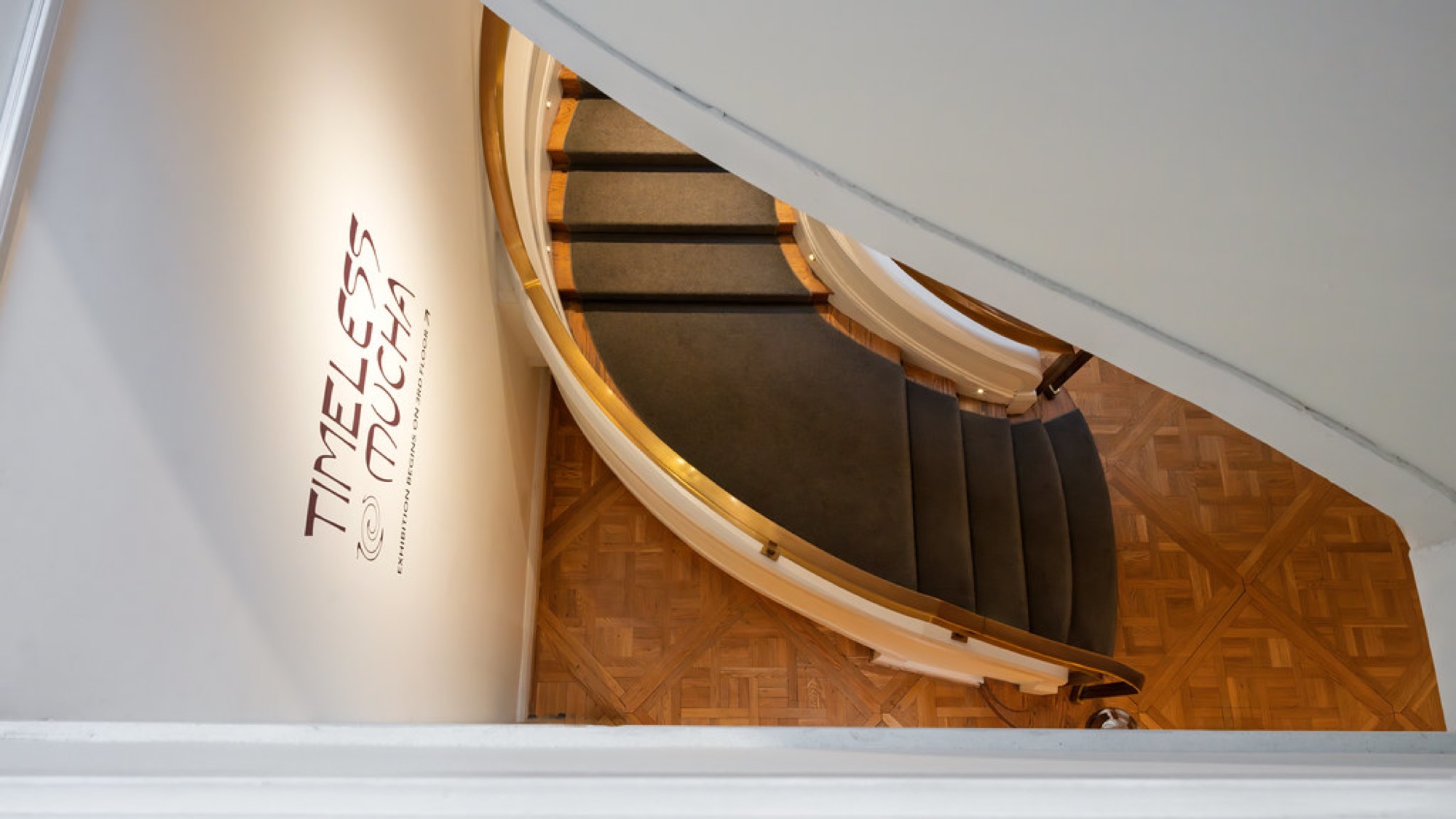A curved staircase seen from above, over a parquet wood floor.